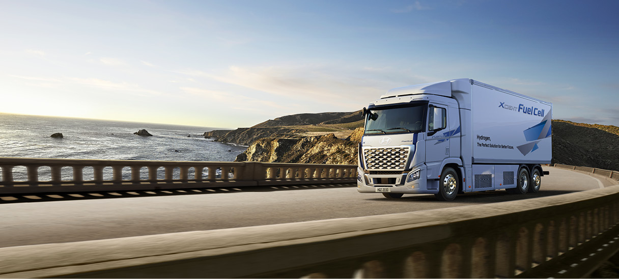 흰색 대형트럭이 교외 도로를 주행하는 전측면 모습