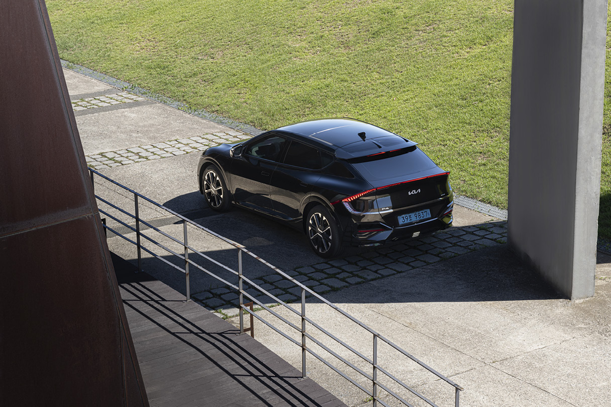 A side view of a black electric car stopping under the shade of a building