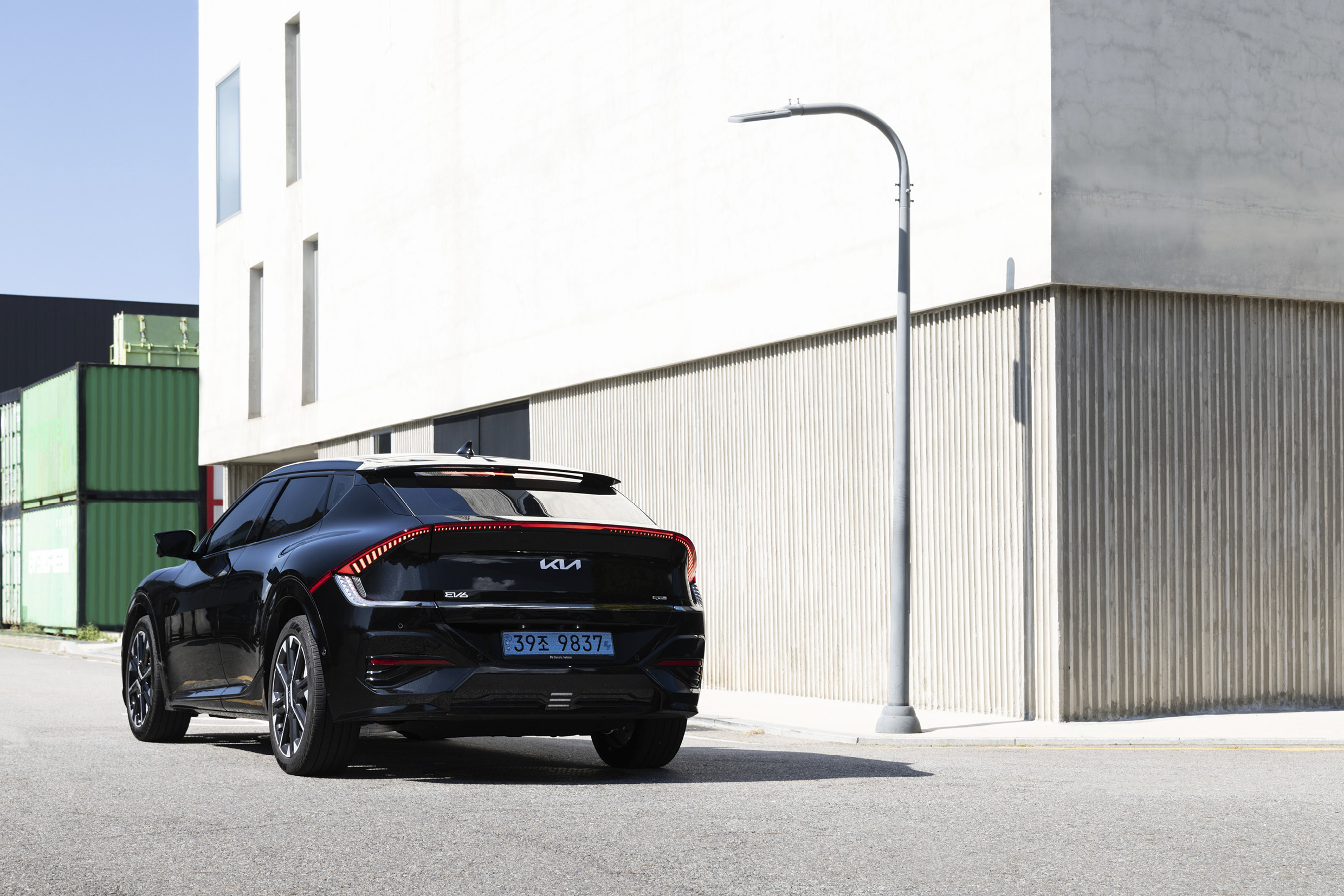 A rear view of a black electric car stopping in front of a white building
