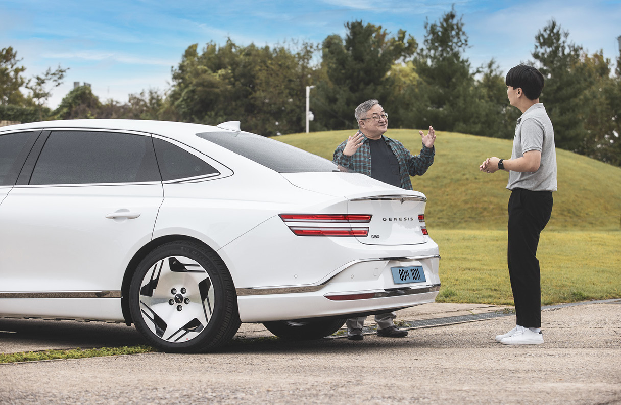 G80 전동화 모델 뒤편에 두 명의 남성이 서서 대화하는 모습