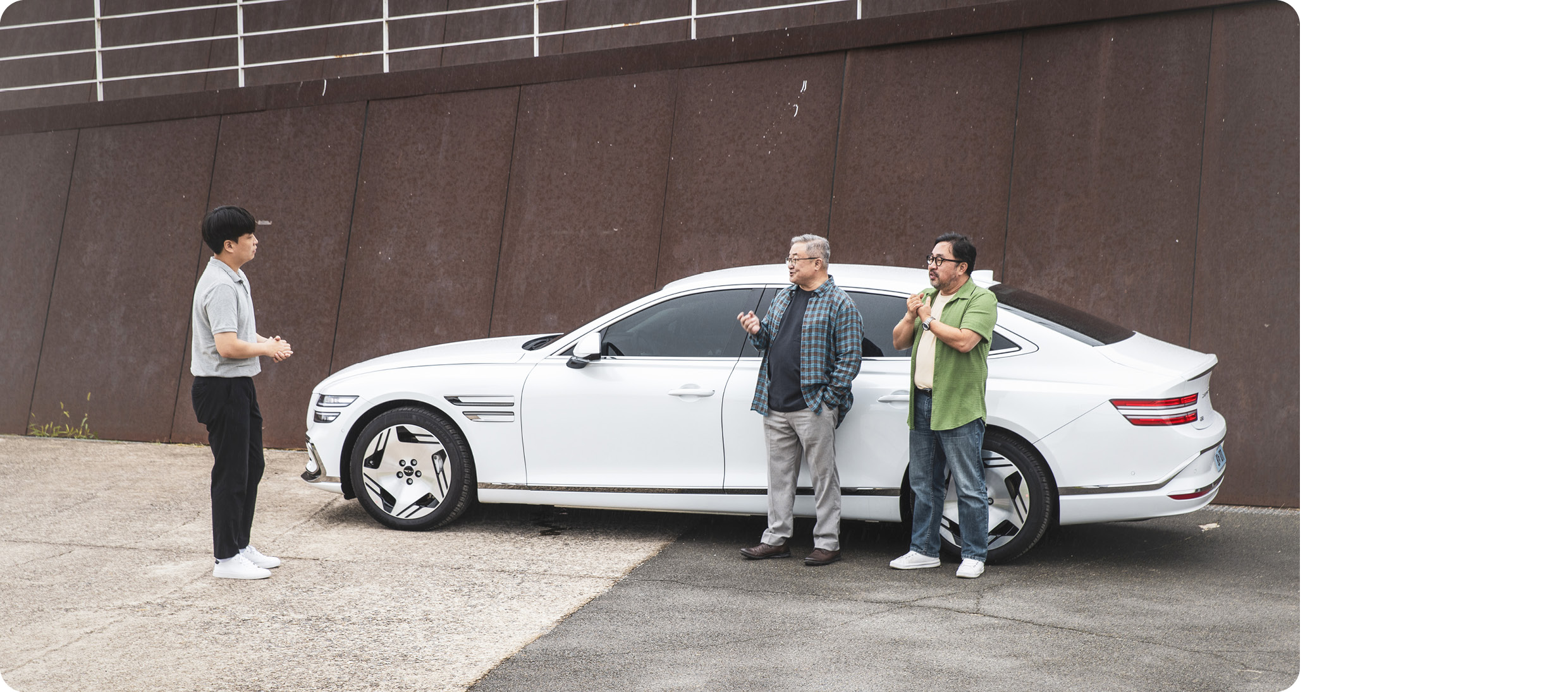 세 명의 남성이 G80 전동화 모델 측면에 서서 대화하는 모습