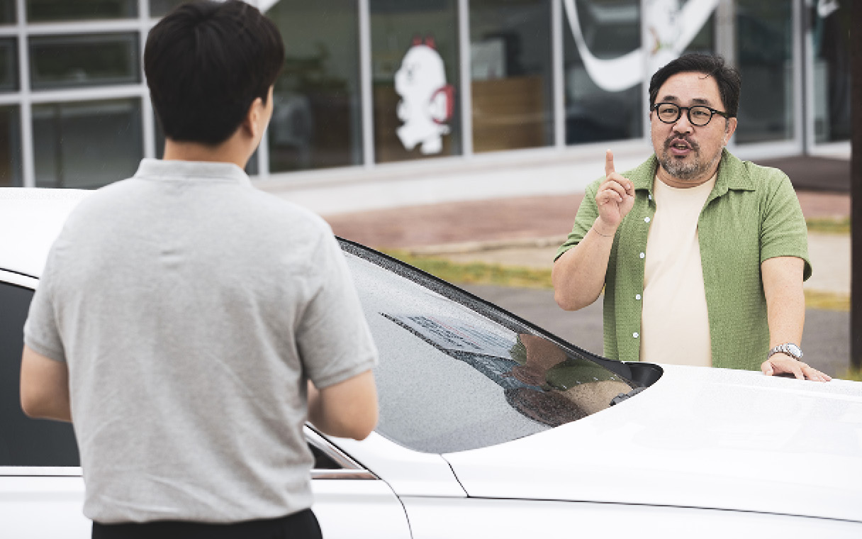 흰색 차 사이에서 두 명의 남성이 마주 보고 대화하는 모습