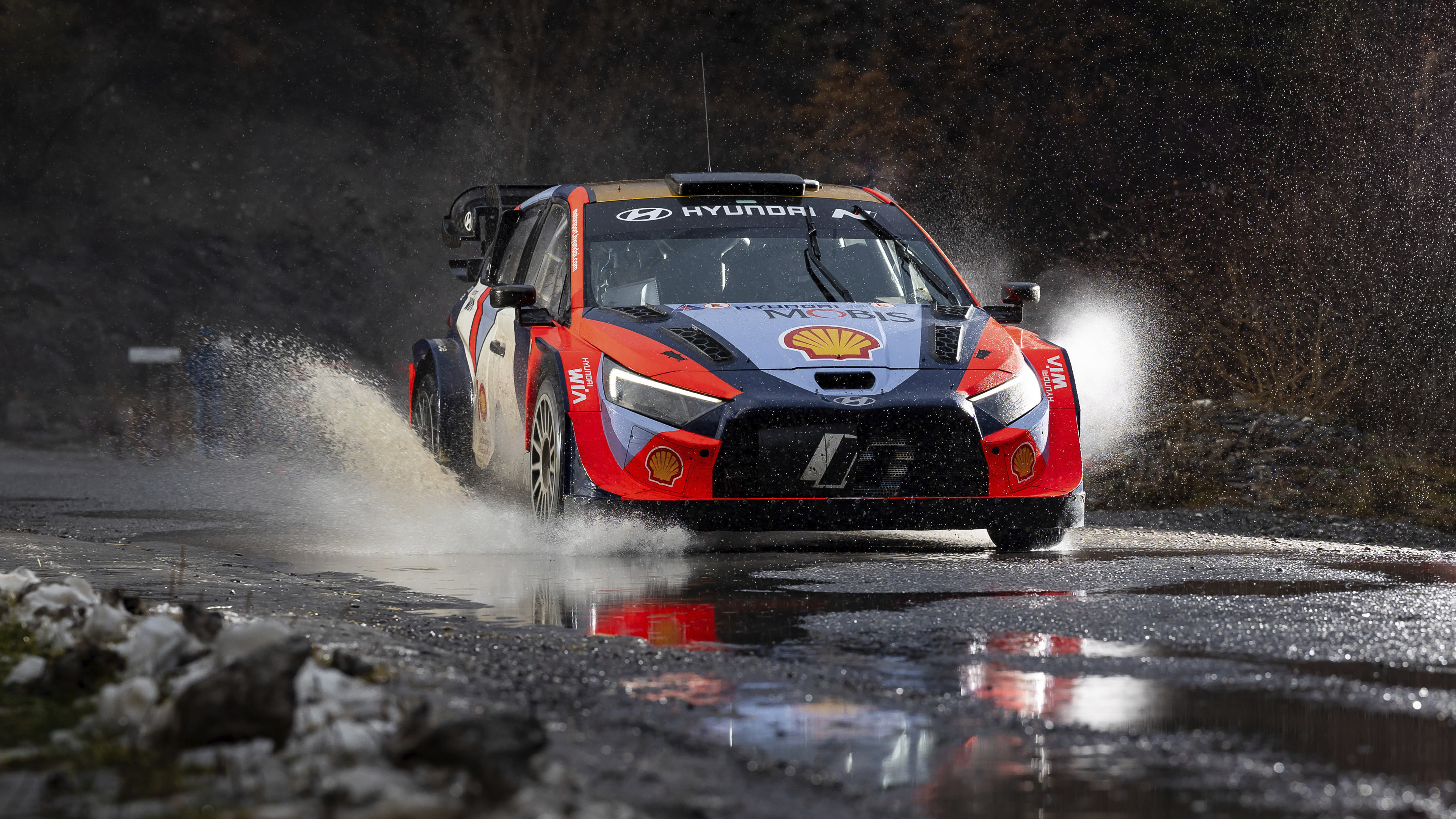 A Hyundai rally car is speeding along a wet road