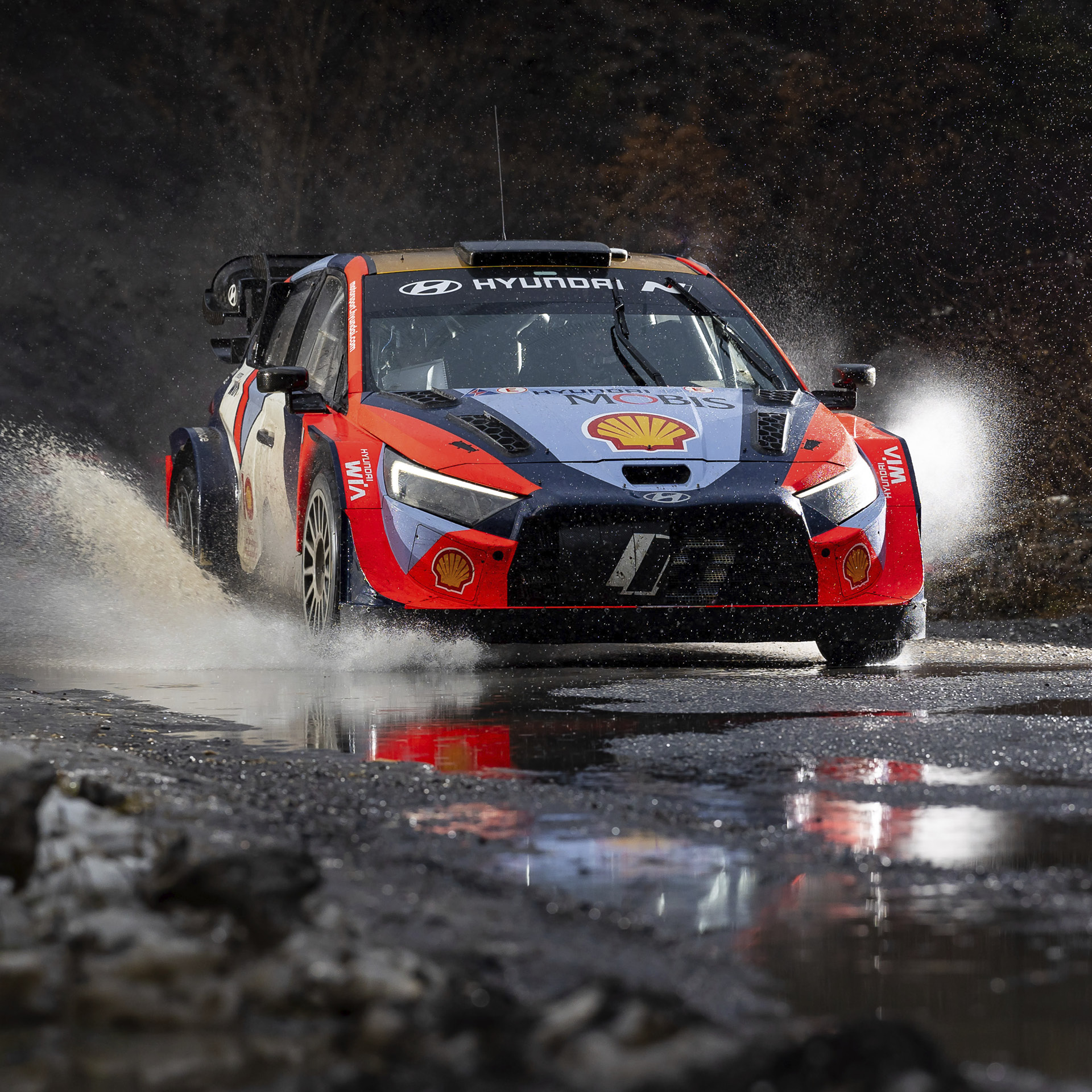 A Hyundai rally car is speeding along a wet road