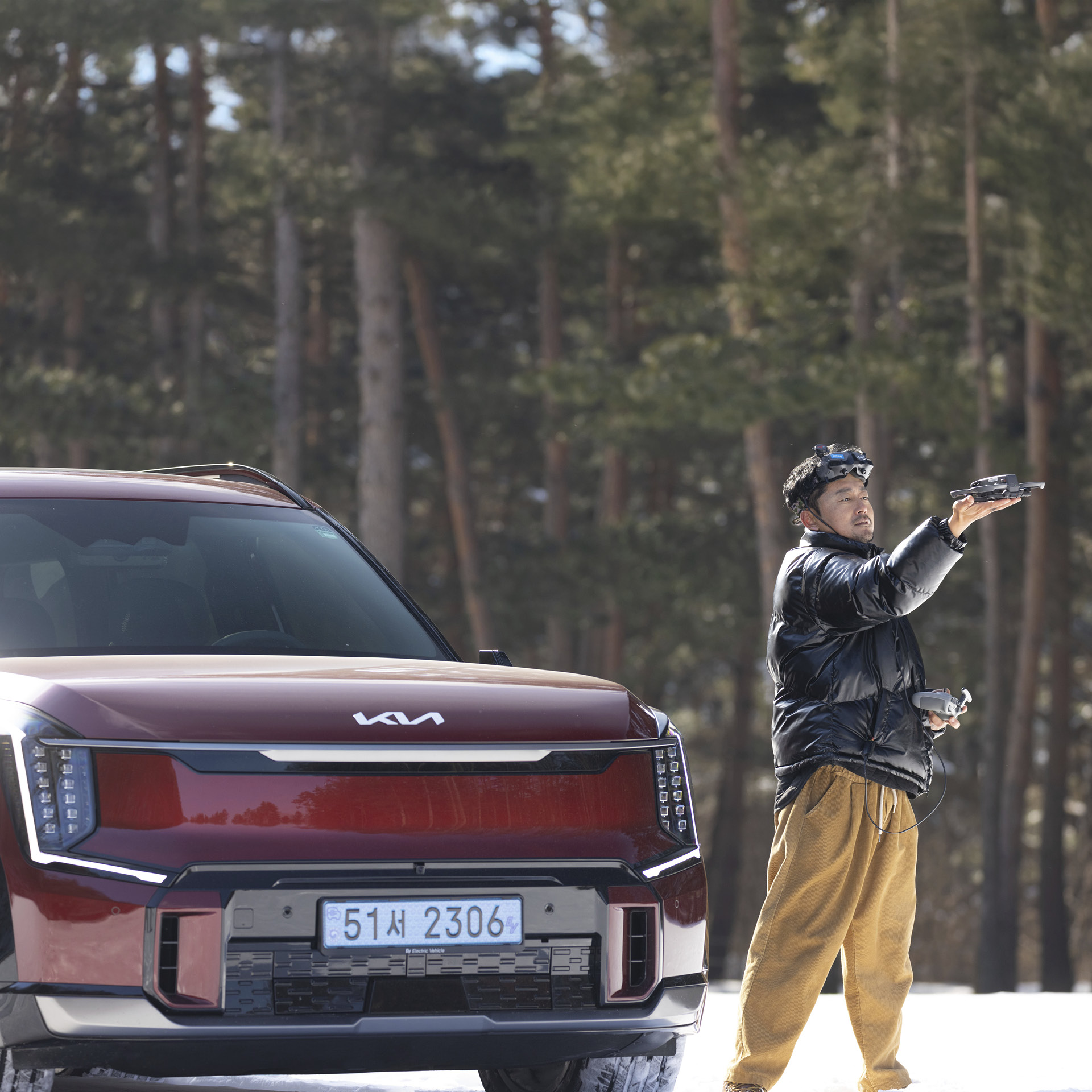 눈 위에 있는 기아 EV9과 드론 촬영 감독의 모습