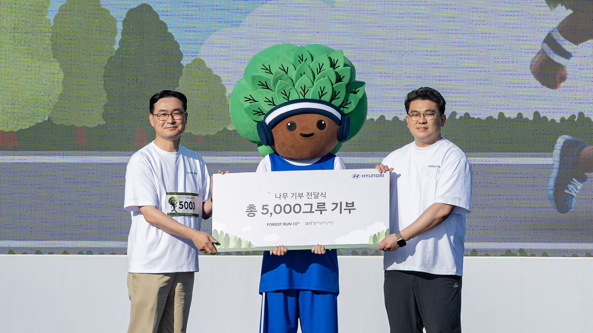 현대자동차 국내사업본부 정유석 부사장, 함께일하는재단 이원태 사무국장, ‘포레스트런’의 새로운 마스코트 ‘그루’가 식재 기부 전달식 기념 촬영을 하는 모습