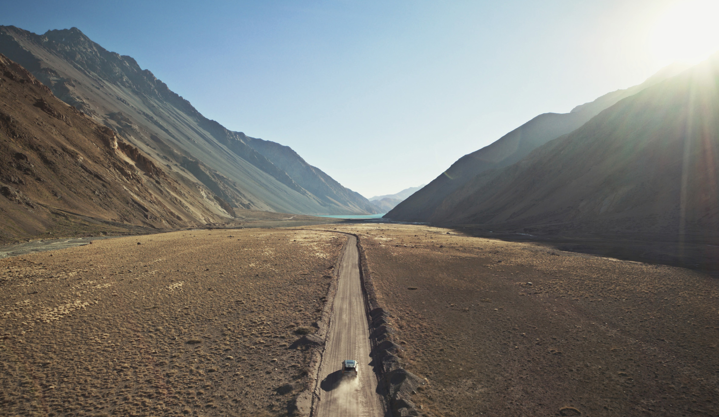 자동차 한 대가 넓게 펼쳐진 자연 속의 도로 위를 달리고 있다