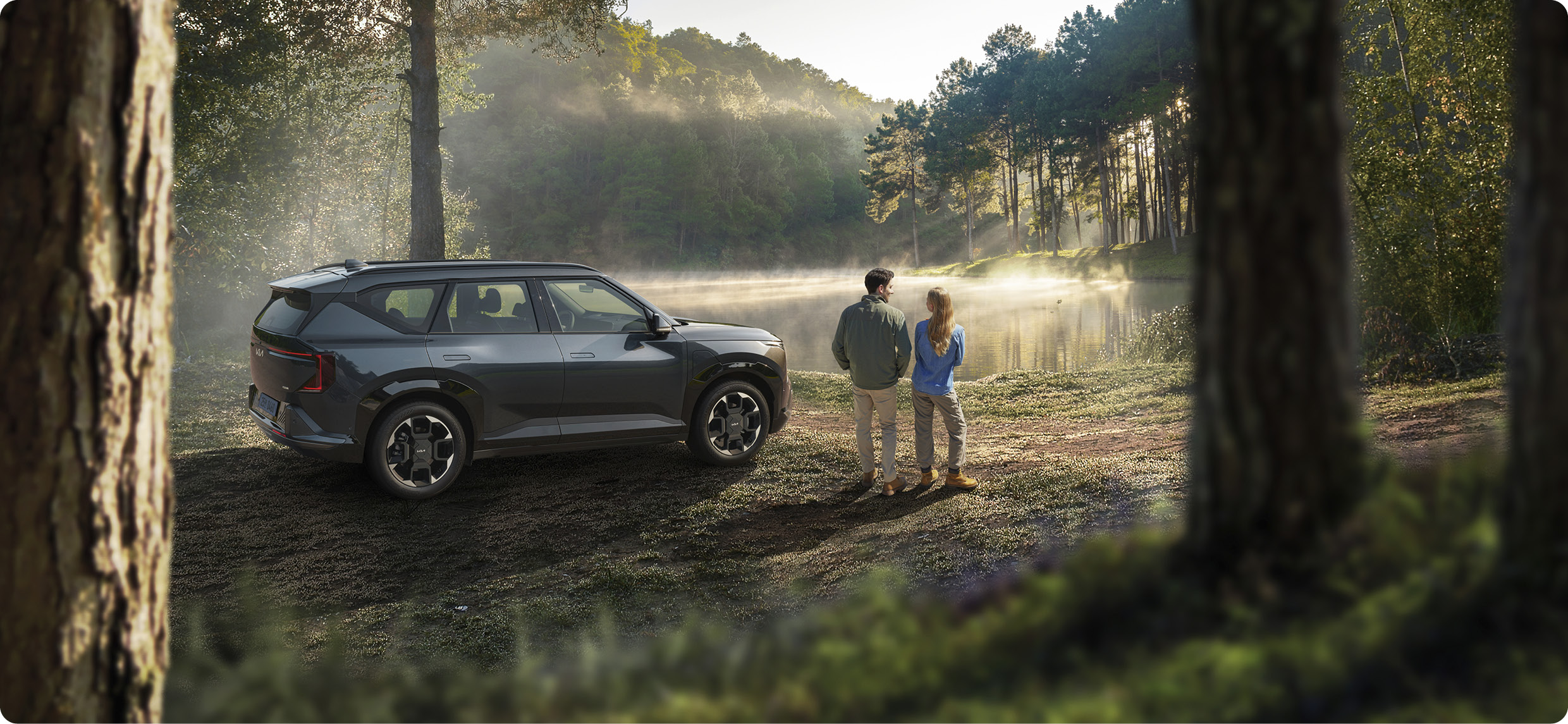 숲에 EV5가 정차하고, 차량 우측면에 남녀 2명이 서 있는 모습