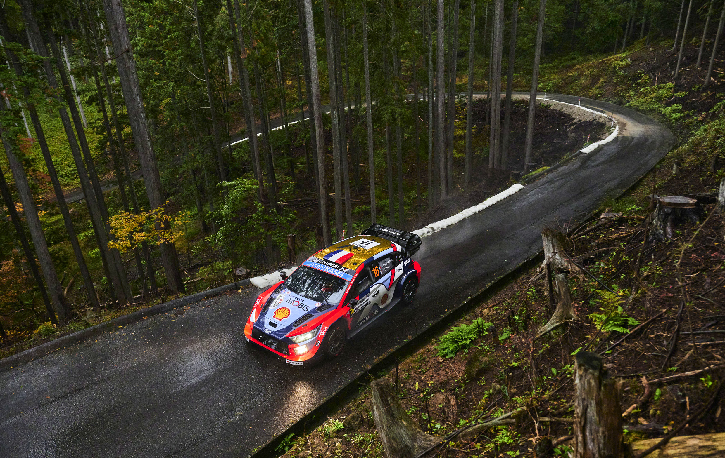 Hyundai Team's rally car driving down a narrow road densely packed with trees
