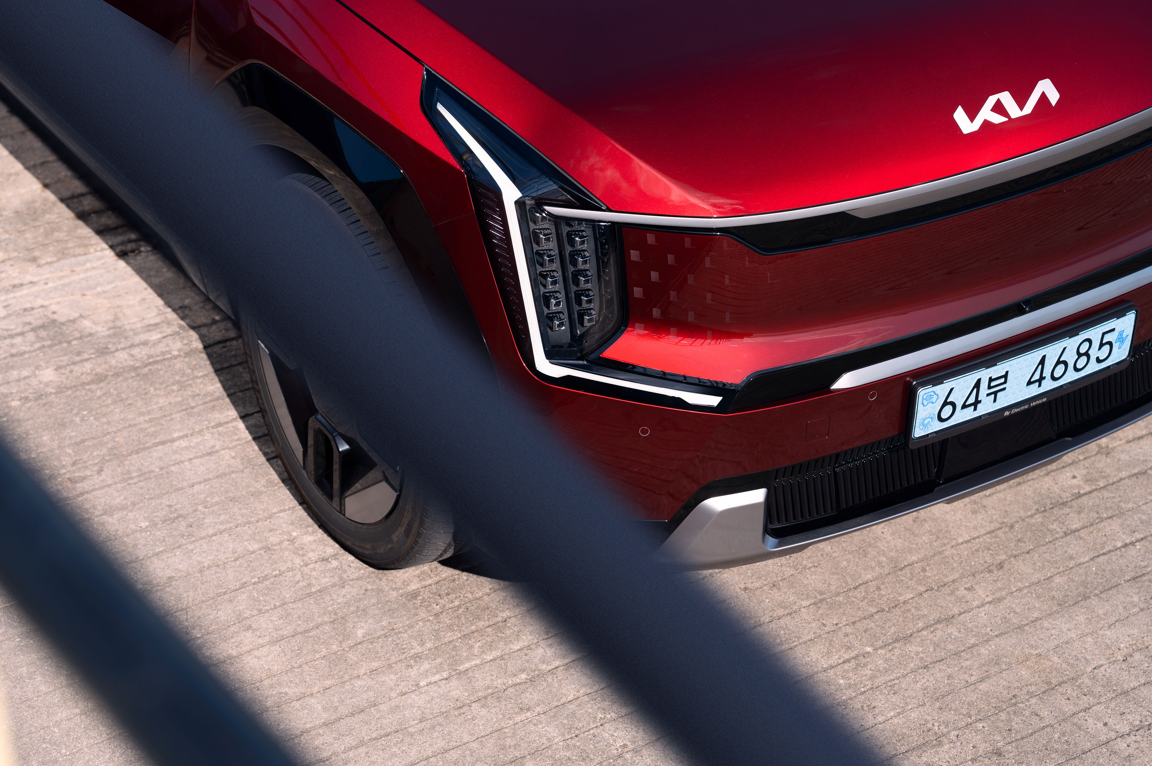 콘크리트 바닥 위에 주차된 기아 EV9의 전면부에 검은색 난간이 왼쪽에 사선으로 걸쳐짐.