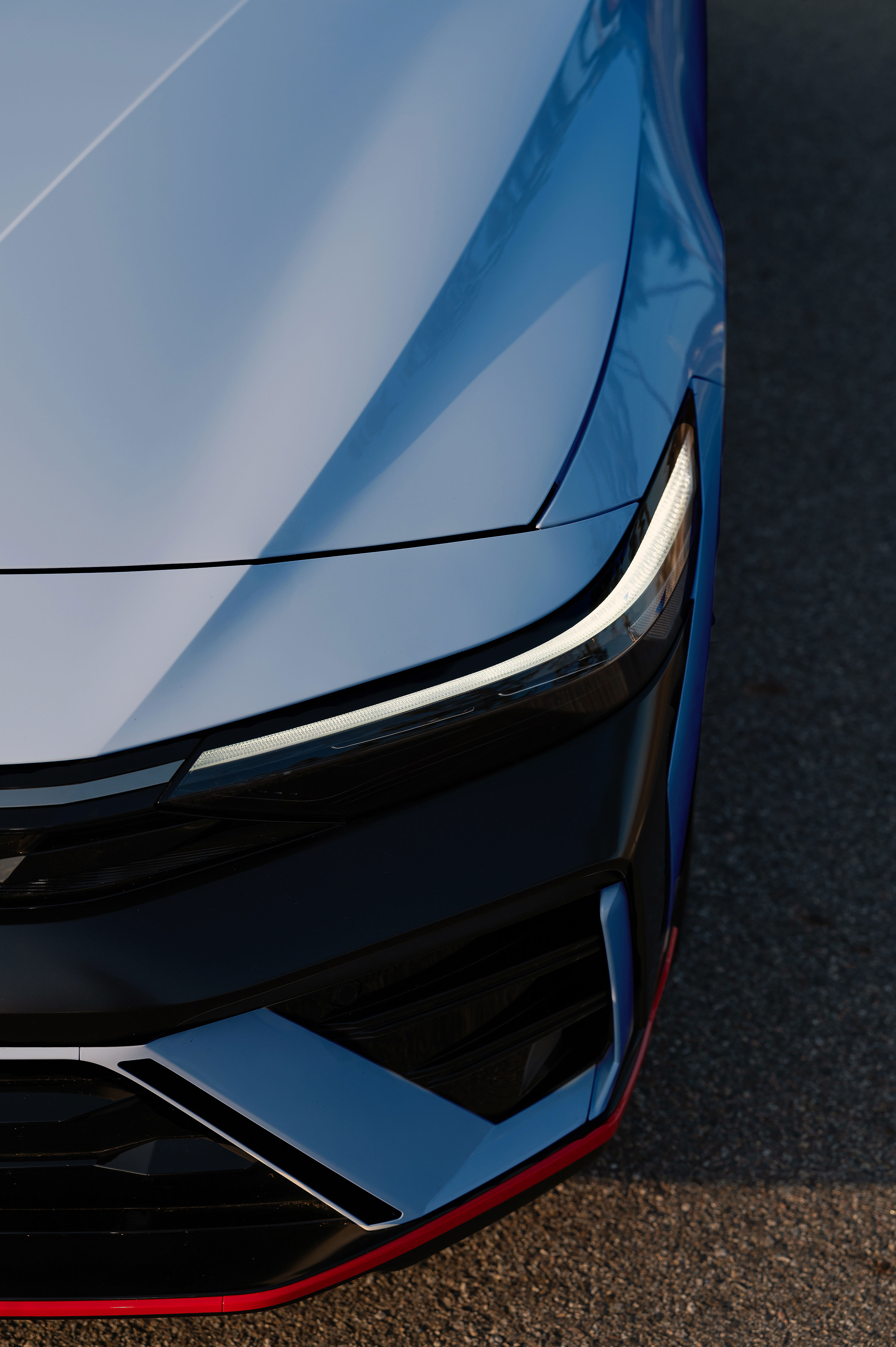 하늘색 더 뉴 아반떼 N 차량의 전면부 헤드라이트와 범퍼가 부분 확대