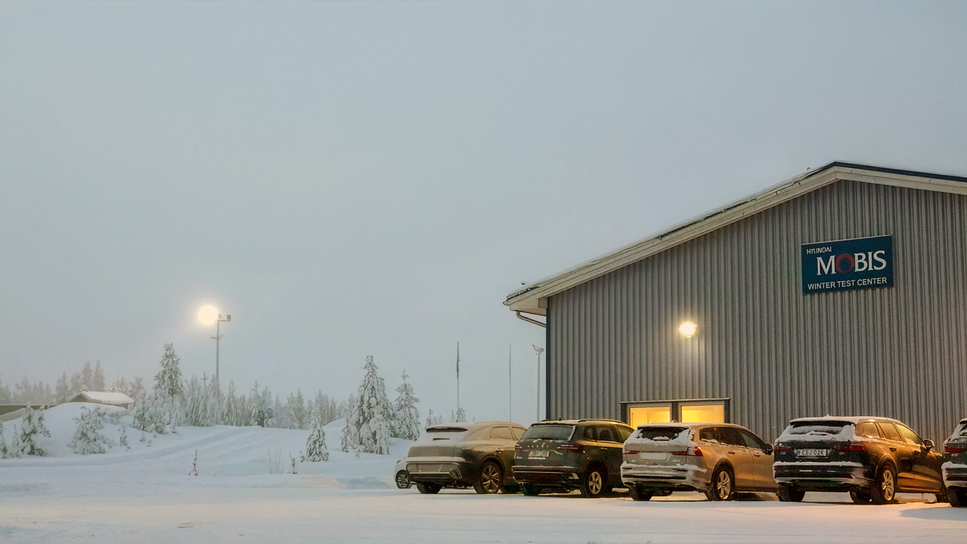 Winter testing facility building at Hyundai Mobis with test vehicles parked on a snowy evening