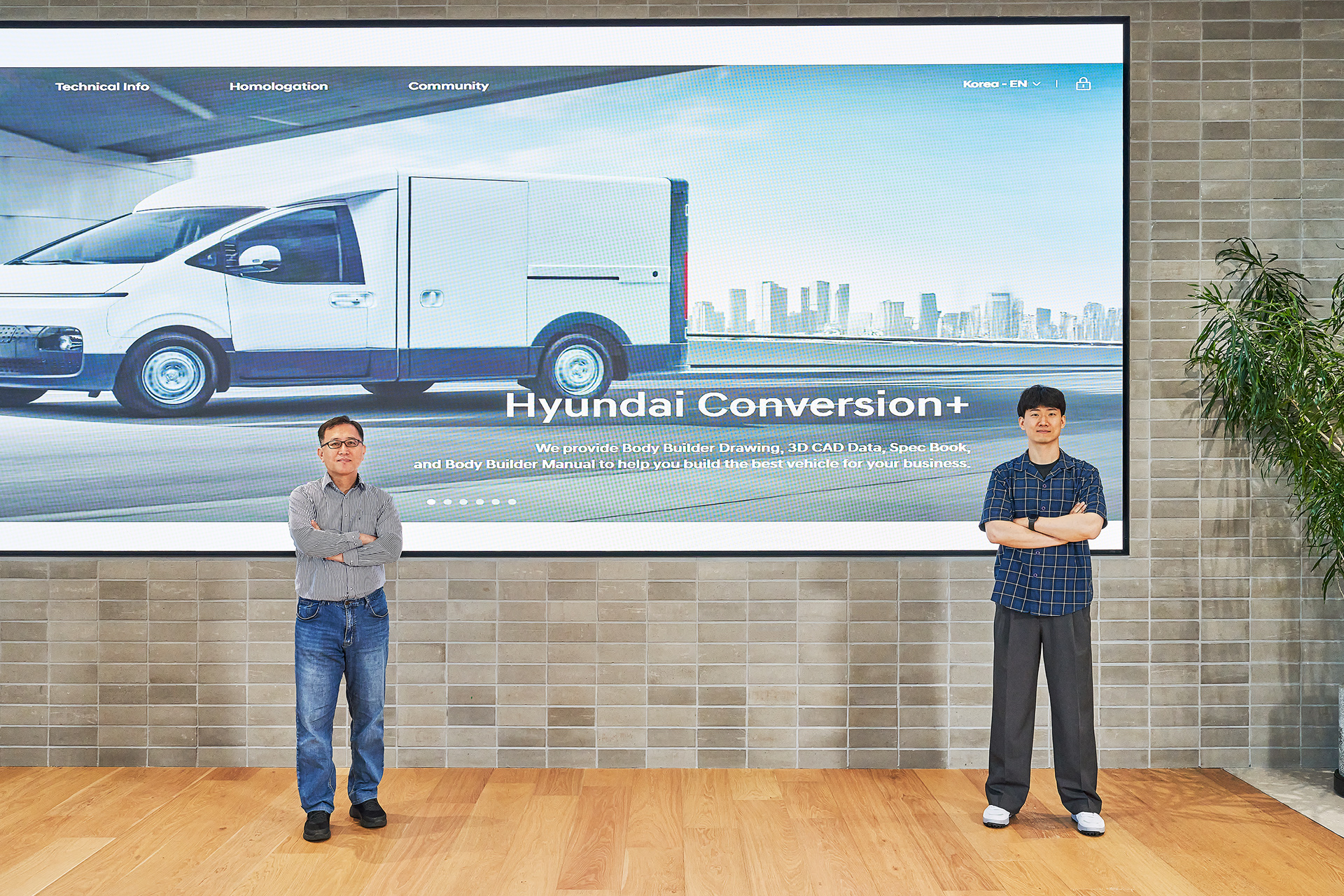 Jung Min-seop and Jeong Seung-jin posing in front of a large digital screen displaying a special-purpose vehicle