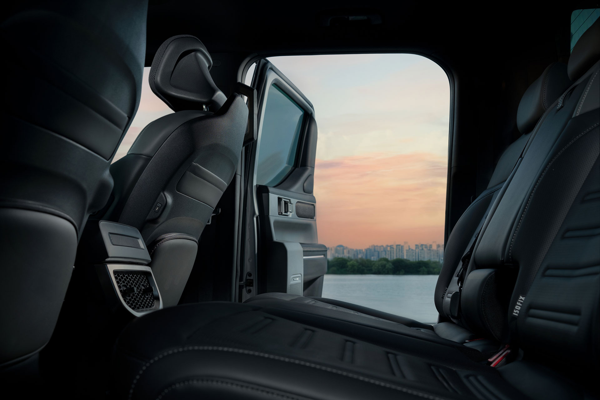 Black leather vehicle interior seen through an open door toward a sunset riverside landscape