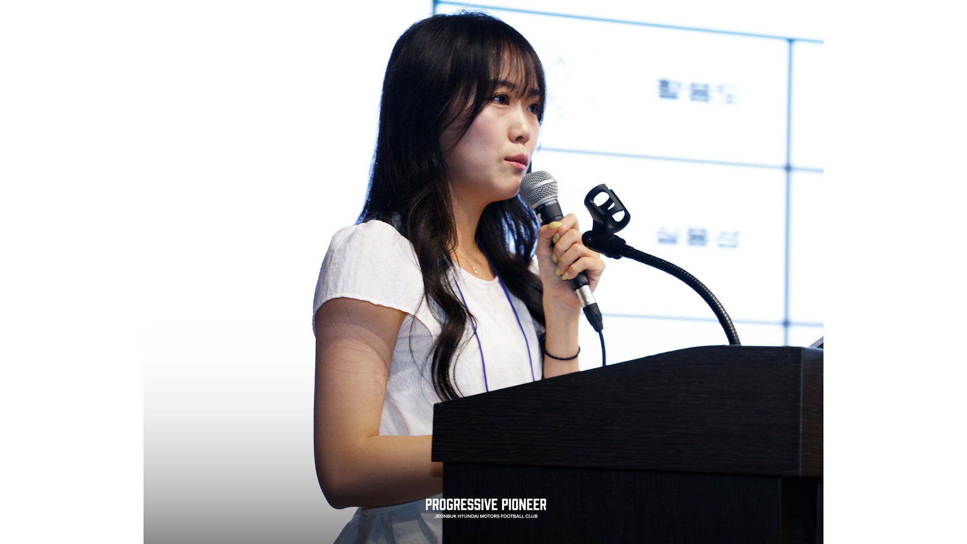 흰 상의의 여성이 단상에서 발표하는 모습