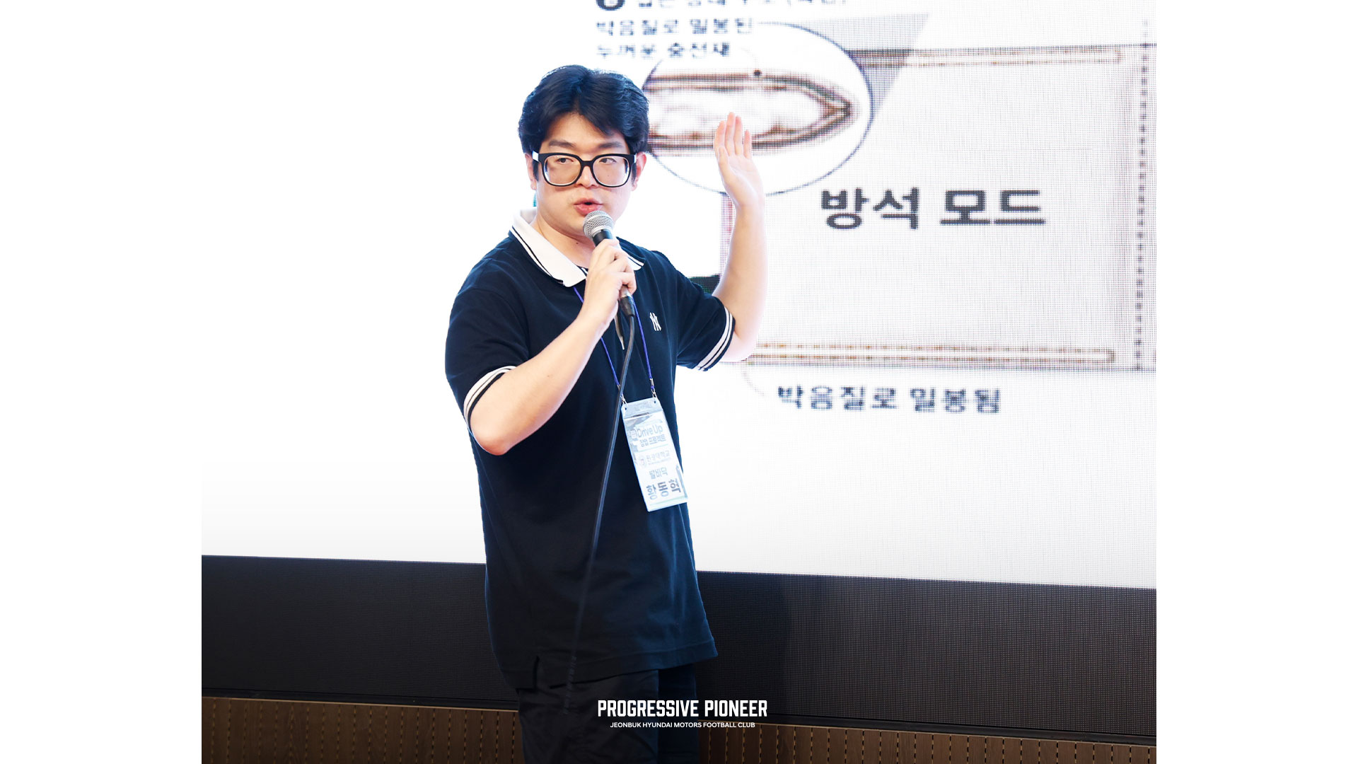 남성이 무대에서 화면을 가리키며 발표하는 모습
